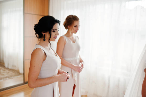istock Helpful bridesmaids looking at a bride while she dresses up. 825604296