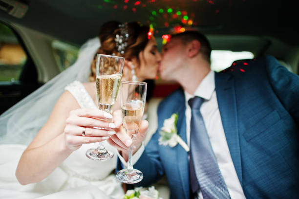 newly married couple drinking champagne in the limousine on their wedding day. - limousine imagens e fotografias de stock