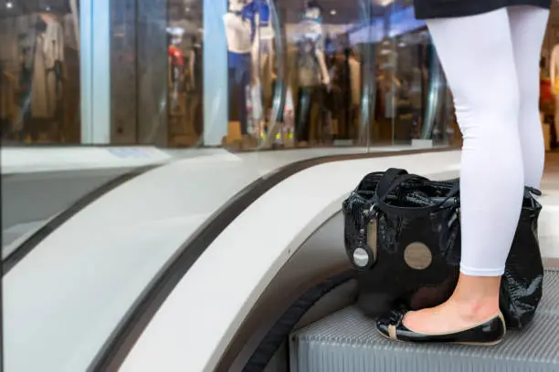Woman standing in flat shoes  with purse on the floor in white legging on escalator in new shoppingmall