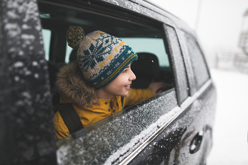 Boy looking through the car window while going on the roadtrip in winter