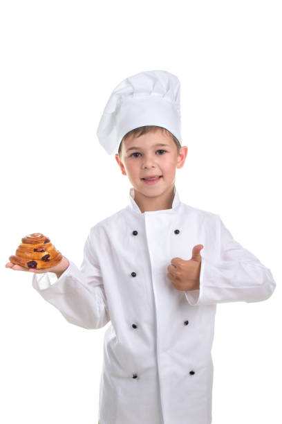 istock Kid in chef uniform with tasty raisin bun gesturing okay, isolated on white 825646810