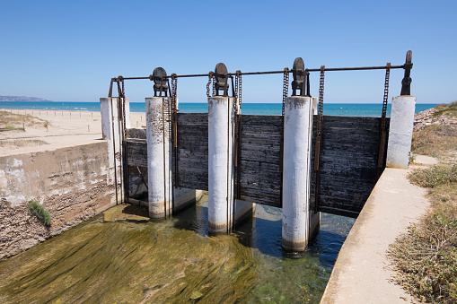 ancient sluices in waterway river towards Mediterranean Sea, next to Gurugu Beach in Castellon, Valencia, Spain, Europe. Blue clear sky