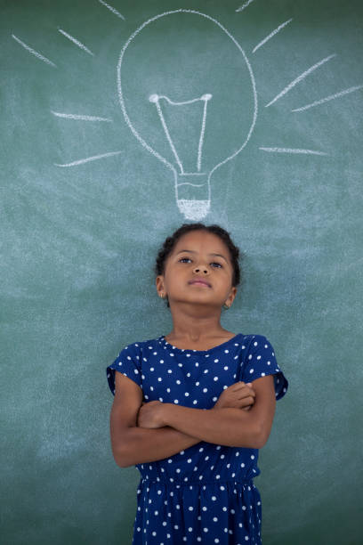 istock Girl with arms crossed standing by bulb drawing on wall 825654628