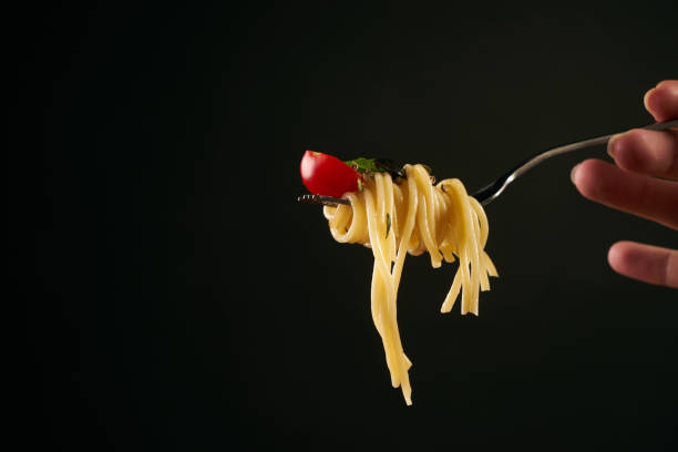 istock Spaghetti on a fork, spaghetti with cherry tomato and fresh basil isolated on black background with copy space. 825680712