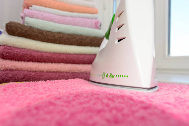 istock Ironing linen with iron. A stack of ironed towels lying next to the iron. Hot iron on an Ironing Board. Teflon sole plate covered with small holes 825688604