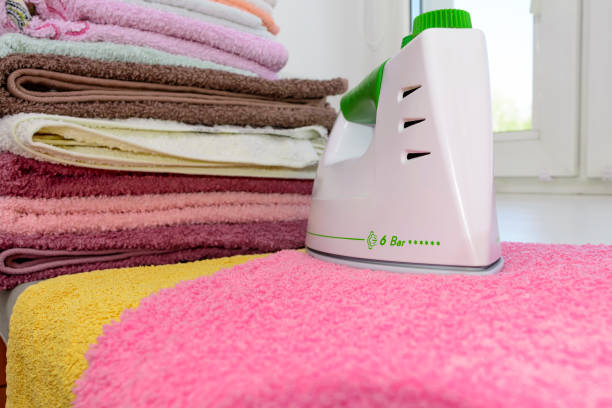 istock Ironing linen with iron. A stack of ironed towels lying next to the iron. Hot iron on an Ironing Board. Teflon sole plate covered with small holes 825688716