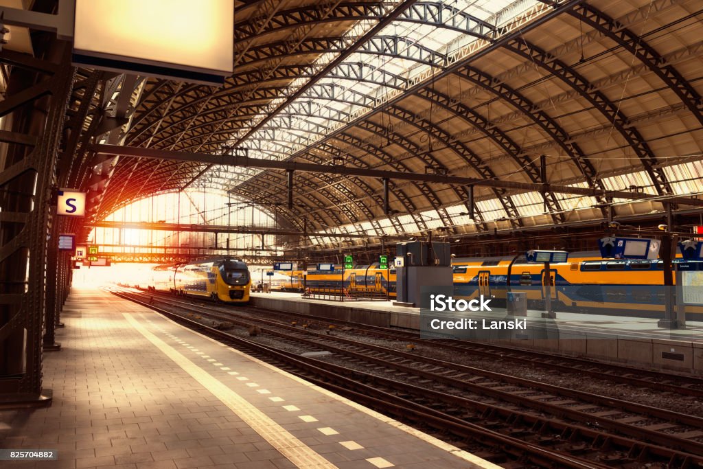 Railway station at rays of sunset Modern railway station with high speed train arriving to the platform at rays of sunset. Amsterdam Central Station. Industrial background. Vintage effect Rail Transportation Stock Photo