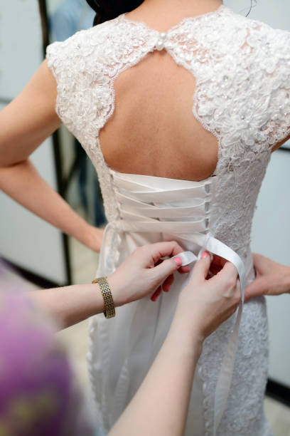 istock Bridesmaid is lacing white wedding dress for beautiful bride 825710528
