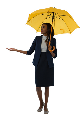 Smiling businesswoman holding umbrella while standing against white bcakground
