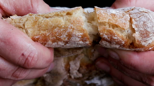 Slow motion of hands breaking a freshly baked loaf of bread