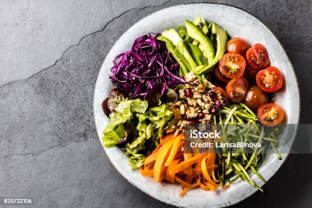 Vegan Buddha Bowl Bowl With Fresh Raw Vegetables Cabbage Carrot Zucchini Lettuce Watercress Salad Tomatoes Cherry And Avocado Nuts And Pomegranate Stock Photo - Download Image Now