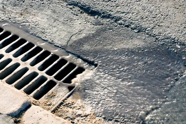 Photo of Water flows down through the manhole cover on a sunny spring day