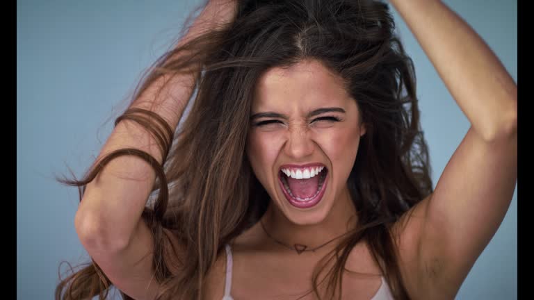 4K video footage of a beautiful young woman touching her long hair in studio against a blue background