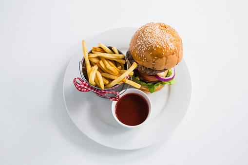 High angle view of burger by french fries in container with tomato sauce on plate against white backgroun