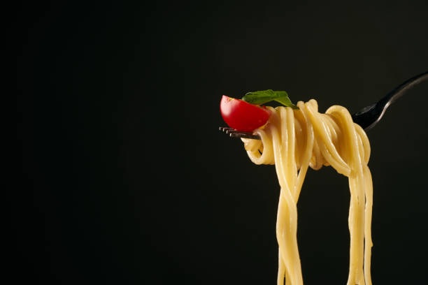 istock Spaghetti on a fork, spaghetti with cherry tomato and fresh basil isolated on black background with copy space 825794134