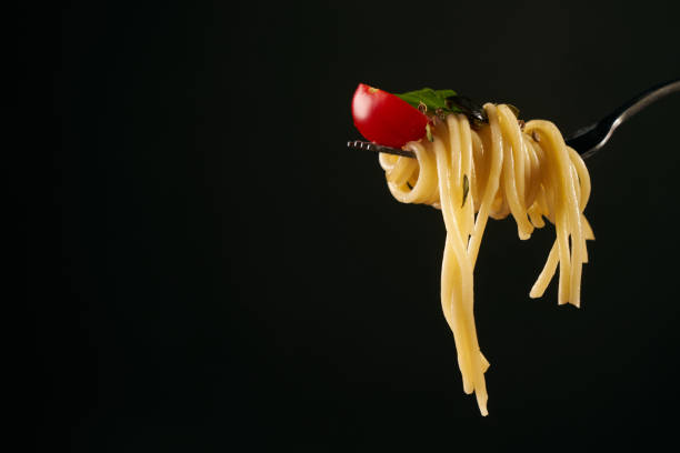 istock Spaghetti on a fork, spaghetti with cherry tomato and fresh basil isolated on black background with copy space. 825796510