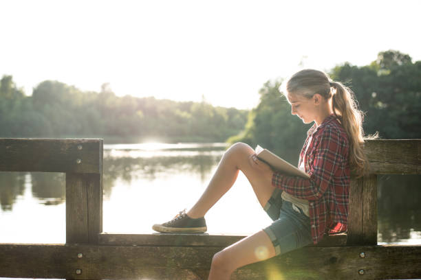 istock Girl reading a book at the lake 825810666