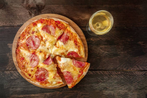 istock Pepperoni pizza with slice cut off, white wine, and copyspace 825815190