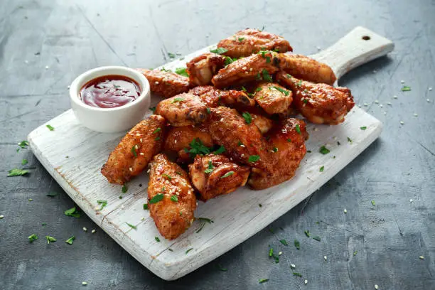 Photo of Baked chicken wings with sesame seeds and sweet chili sauce on white wooden board.