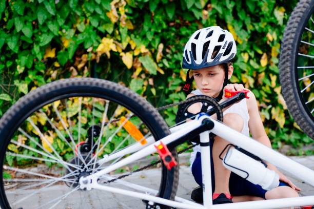 ragazzo felice con un casco da bicicletta che ripara la sua bici - bicycle chain foto e immagini stock
