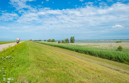 Woman riding a scooter on a dike along a lake in summer