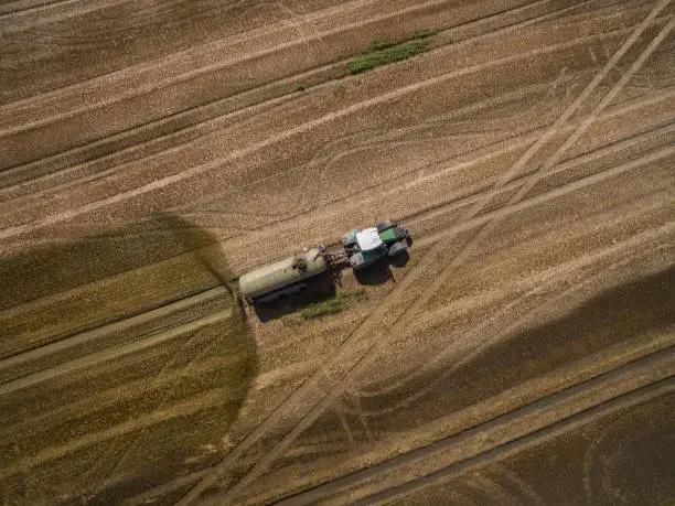 aerial view of a tractor with a trailer fertilizes a freshly plowed agriculural field with manure in germany