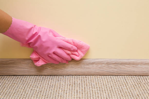 hand in schützende gummihandschuh mit mikrofaser-tuch reinigung fußleiste auf dem boden von staub an der wand. zeitigen frühjahr reinigung oder regelmäßig aufräumen. zimmermädchen reinigt haus. - lappen reinigungsgeräte stock-fotos und bilder