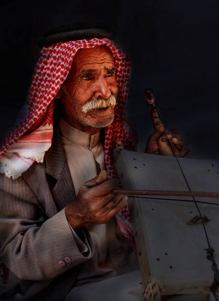 viejo hombre beduino u hombre árabe en traje tradicional, tocando su instrumento musical en la puerta de la pequeña petra. - siq al barid fotografías e imágenes de stock