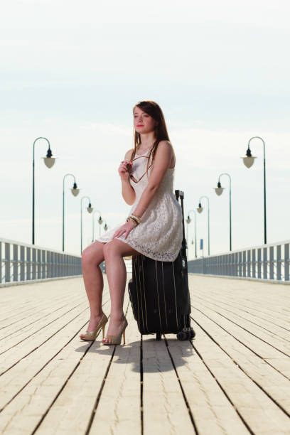 istock Woman sitting on suitcase, pier in background 825837774