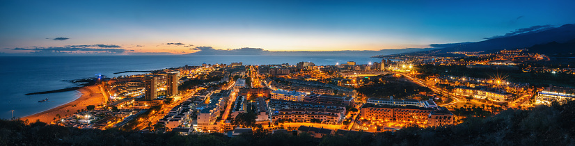 Panoramic view of the Illuminated Las Americas at night against the colorful sunset sky with lights on the horizon on Tenerife island, Spain