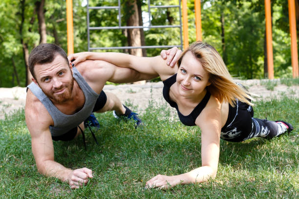 istock Young blond girl and bearded man doing exercise plank in park together. 825846802