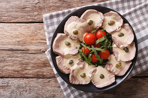 Italian cuisine: Vitello tonnato with capers, arugula, tomatoes on a plate close-up. horizontal view from above