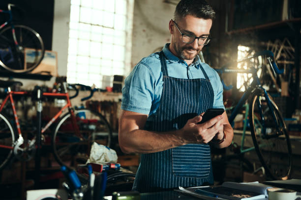 Keeping his customers updated with the progress Shot of a mature man working in a bicycle repair shop bicycle shop stock pictures, royalty-free photos & images