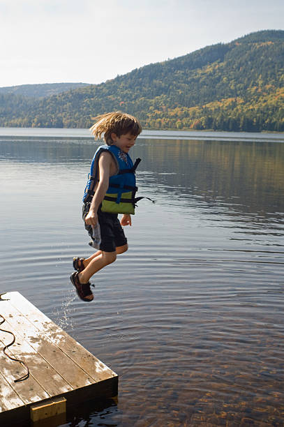 boy jumping off dock into lake - life jacket little boys lake jumping foto e immagini stock