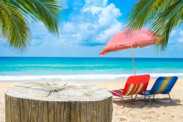 Wooden desk or stump on sand beach in summer,Beach chairs with umbrella  background.