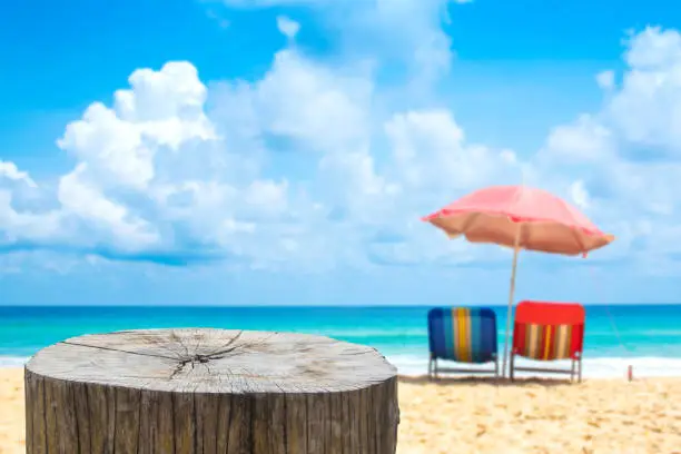 Wooden desk or stump on sand beach in summer,Beach chairs with umbrella  background.
