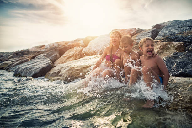 istock Children sitting  on sea groyne having fun being splashed by water 825878526