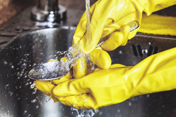 istock Hands in yellow rubber gloves, wash spoon in sink 825878568