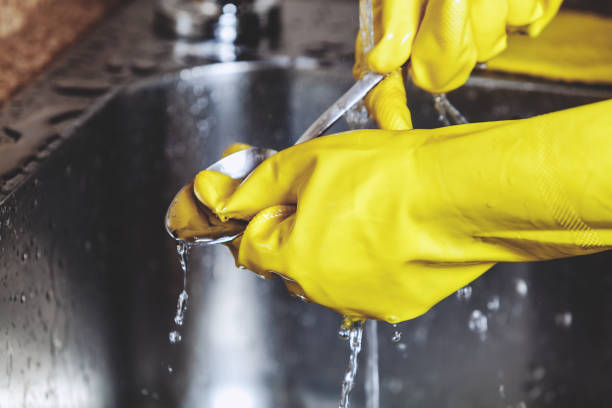 istock Hands in yellow rubber gloves, wash spoon in sink 825878604