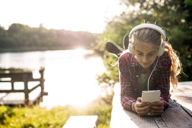 ragazza che usa lo smartphone al lago - music listening child smiling foto e immagini stock
