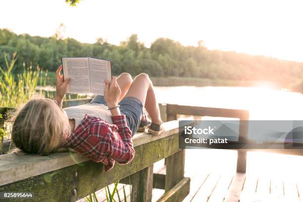 Photo libre de droit de Jeune Fille Lisant Un Livre Au Bord Du Lac banque d'images et plus d'images libres de droit de Lire - Lire, Enfant, Été