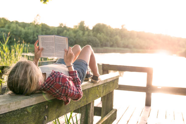 ragazza che legge un libro al lago - enjoying a novel foto e immagini stock