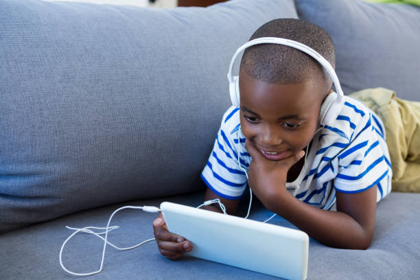 istock Boy using digital tablet while listening to headphones on sofa at home 825898722