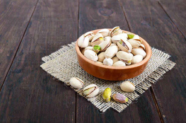 istock Useful nuts - pistachios in a ceramic bowl on a dark wooden background. 825925728