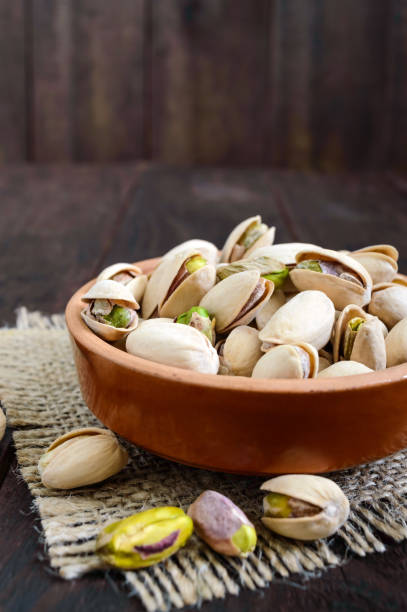 istock Useful nuts - pistachios in a ceramic bowl on a dark wooden background. Vertical view 825925740