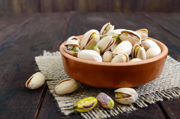 istock Useful nuts - pistachios in a ceramic bowl on a dark wooden background. 825925784
