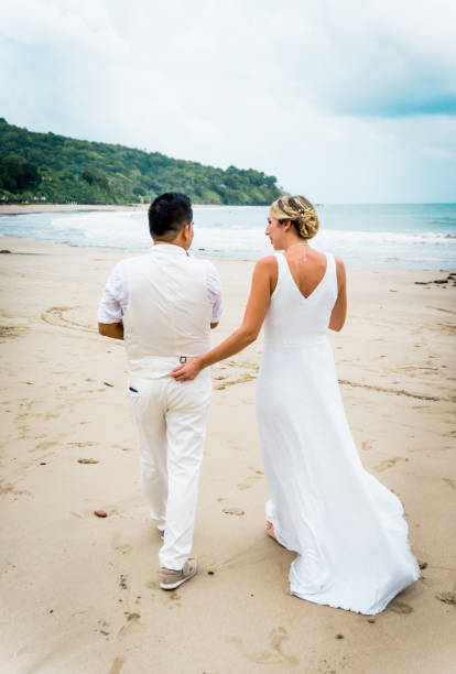 istock Bride and Groom Walking holding Baby Daughter on Beach 825928032