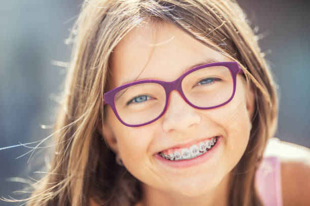 heureuse jeune fille souriante avec bretelles dentaires et les lunettes. jeune fille blonde caucasienne mignonne vêtu d’accolades de dents et lunettes - dentists chair people care medical equipment photos et images de collection