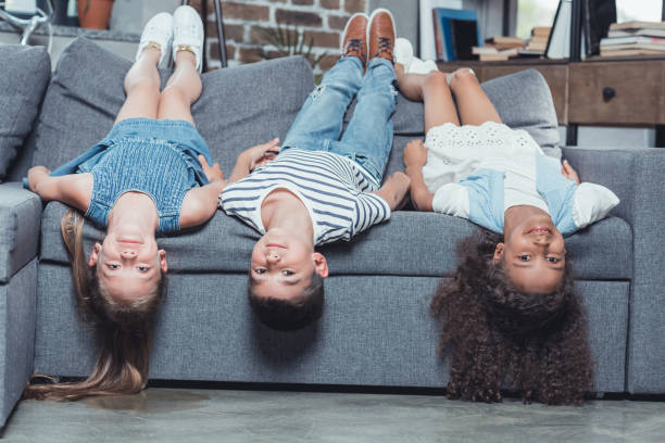 istock multiethnic smiling children looking at camera while lying on sofa at home 825941156