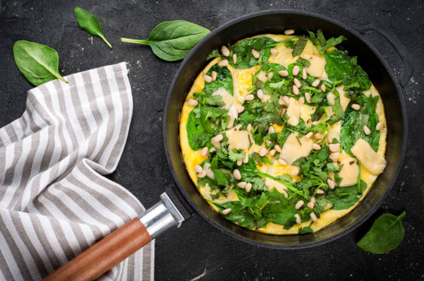 istock Omelet with eggs, spinach, pine nuts and vegetables. Spinach tortilla in pan on dark background.  Delicious breakfast or appetizer snack 825961336